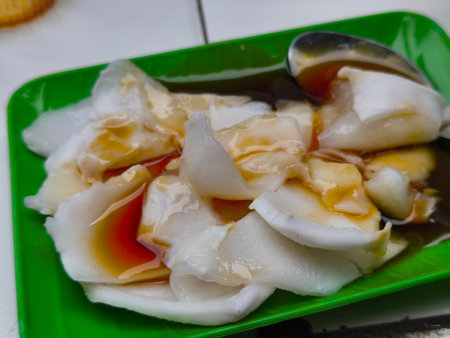 Close-up of a refreshing tropical dessert featuring soft, translucent coconut pieces drenched in sweet brown sugar syrup, served on a bright green plate.の写真素材