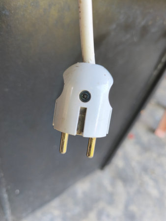 Close-up of a white electrical plug featuring two golden pins, connected to a cable, set against a blurred dark background.の写真素材