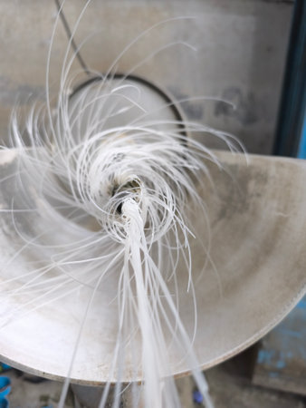 Close-up of numerous thin, white plastic strands in dynamic motion, spiraling into an industrial machine during a manufacturing process. The abstract movement creates a sense of energy.の写真素材