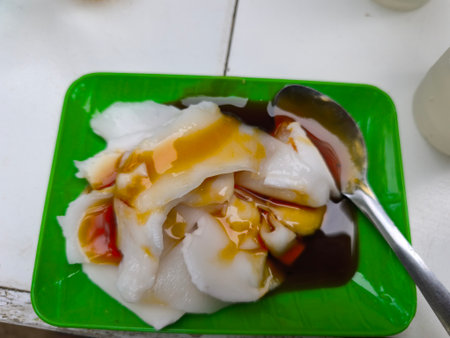 A vibrant green plate holds a serving of white translucent dessert pieces, generously topped with a rich dark sauce and a bright yellow-orange dressing. A silver spoon rests ready to enjoy this sweet treat.の写真素材