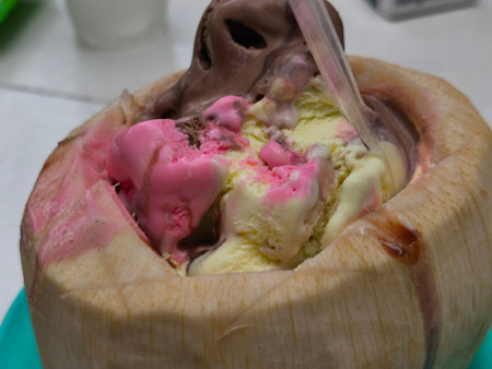 Scoops of colorful strawberry, vanilla, and chocolate ice cream are served inside a refreshing young coconut shell, with a spoon ready to enjoy this tropical dessert.の写真素材