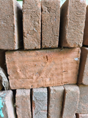 Detailed vertical shot of rough, reddish-brown bricks stacked, emphasizing their natural texture and dusty surface for construction.の写真素材