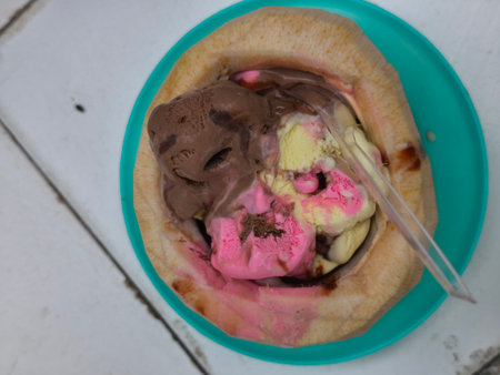 Refreshing scoops of chocolate, pink, and yellow ice cream melt inside a natural coconut shell,...