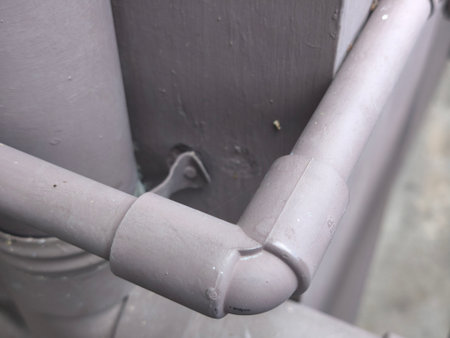 A close-up view of grey PVC pipes forming an elbow joint, securely mounted against a textured grey wall, showcasing building utility lines.の写真素材