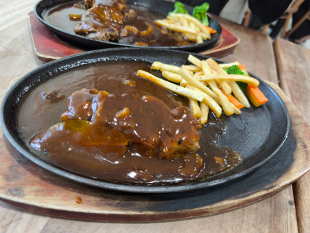 Delicious hot plates of meat steak, smothered in rich brown gravy, served with golden french fries and fresh vegetables on a rustic wooden tableの写真素材