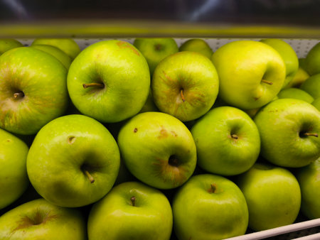 Vibrant green apples are tightly packed together, showcasing their fresh and healthy appearance in a brightly lit market displayの写真素材