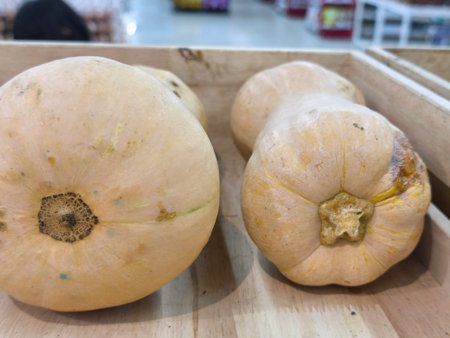 Several light colored butternut squash are arranged in rustic wooden crates, ready for sale in a grocery store settingの写真素材
