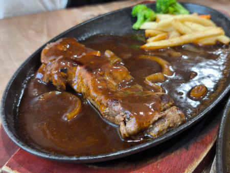 Delicious sizzling steak on a hot cast iron plate, topped with rich brown gravy and onions, served alongside golden french fries and fresh green broccoliの写真素材
