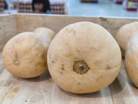 Light colored gourds with subtle markings rest in a rustic wooden crate, ready for sale in a grocery store settingの写真素材