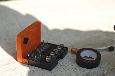 a box with tools, a box with a screwdriver and bits, and electrical tape nearby