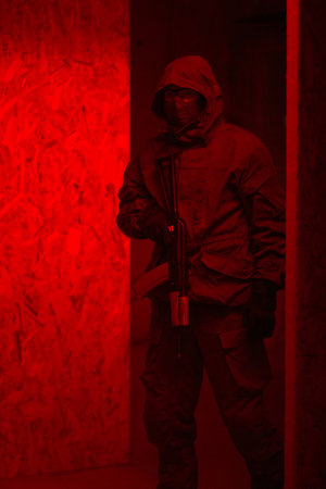 Man in a hood with a gun in his hands in a dark roomの写真素材