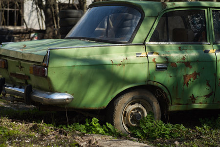 old green car, wheels partially covered with weeds and earth, abandoned vehicleの写真素材