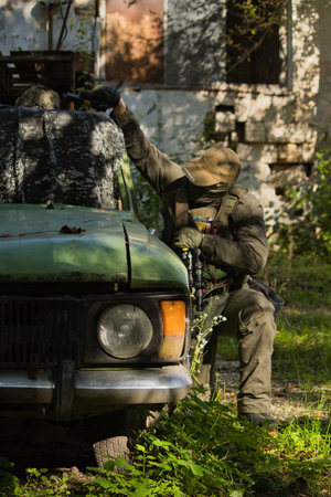 Tactical operator in full combat gear including plate carrier, tactical pants, and cap, holding rifle with optics in urban training environmentの写真素材