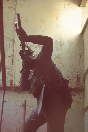 Tactical operator in full combat gear including plate carrier, tactical pants, and cap, holding rifle with optics in urban training environmentの写真素材