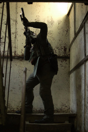 Tactical operator in full combat gear including plate carrier, tactical pants, and cap, holding rifle with optics in urban training environmentの写真素材