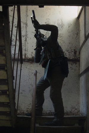 Tactical operator in full combat gear including plate carrier, tactical pants, and cap, holding rifle with optics in urban training environmentの写真素材