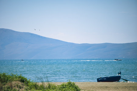 A peaceful summer seascape with turquoise water, distant blue mountains, a small boat on the shore....