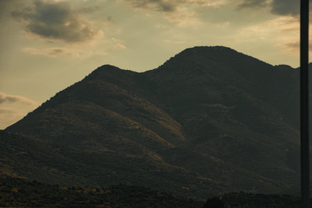A rugged mountain range rises under dramatic layered clouds, creating a moody and atmospheric natural landscape.の写真素材