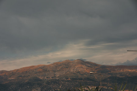 A rugged mountain range rises under dramatic layered clouds, creating a moody and atmospheric natural landscape.の写真素材