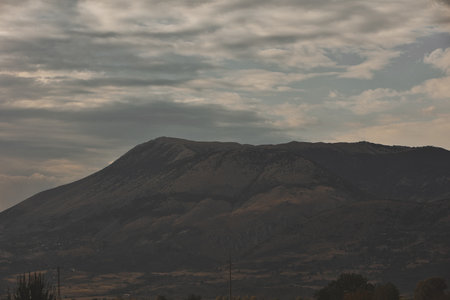 A rugged mountain range rises under dramatic layered clouds, creating a moody and atmospheric natural landscape.の写真素材