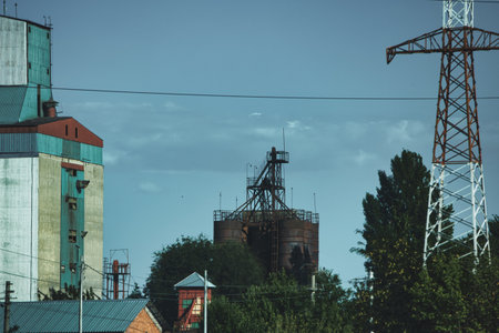 Industrial landscape with old grain elevators, metal silos, and power transmission towers under a clear summer sky, captured during a roadside journey in 29 August 2025.のeditorial素材