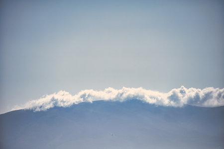 VlorÃ«, Albania â August 21 2025: A scenic view of soft white clouds rolling over distant blue mountains under a clear sky.の写真素材