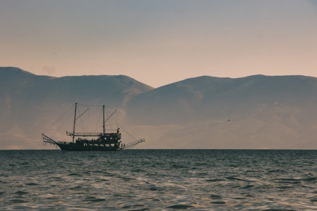 VlorÃ«, Albania August 2025 A tourist boat sails across the calm blue sea with distant mountains forming a soft silhouette on the horizon.の写真素材