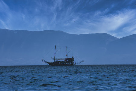 Vlorã¢, Albania August 2025 A tourist boat sails across the calm blue sea with distant mountains forming a soft silhouette on the horizon.の写真素材