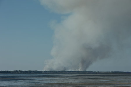 A distant wildfire sends a towering column of smoke into the sky above a small coastal island near Vlora, Albania, captured on August 25, 2025の写真素材