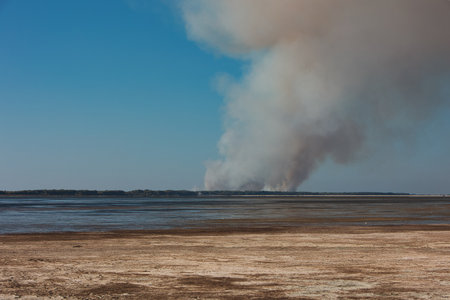 A distant wildfire sends a towering column of smoke into the sky above a small coastal island near Vlora, Albania, captured on August 25, 2025の写真素材