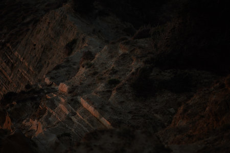 Rocky cliffs in Vlora, Albania, captured on August 25, 2025. The scene is dimly lit by the last light of sunset, highlighting the rugged texturesの写真素材