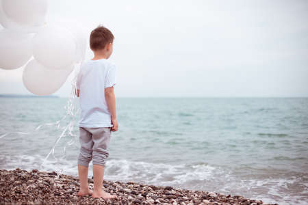lonely Boy in a White Dress with White Balloonsの写真素材