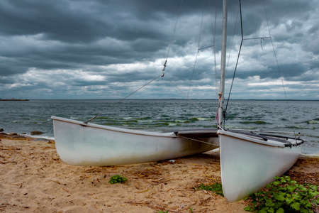 A white catamaran pulled ashore on a cloudy day. Dark, heavy sky.Frombork, Poland.