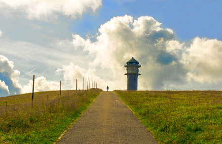 way to a tower in the green grass and clouds on mountainの写真素材