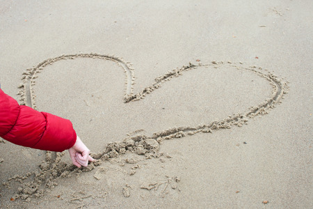 child is drawing in the sand  a heartの写真素材