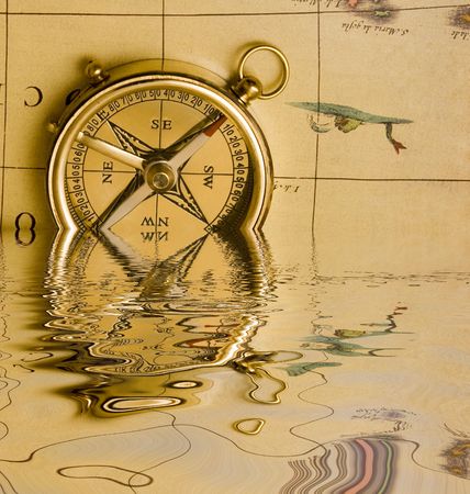 Old style brass compass on antique  map with reflection on waterの写真素材