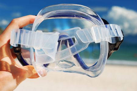 Snorkel equipment in hand against beach and skyの写真素材