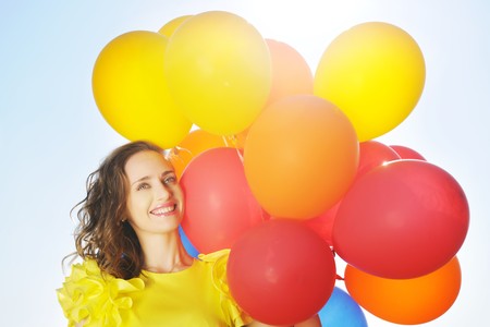 Woman holding balloons against sun and skyの写真素材