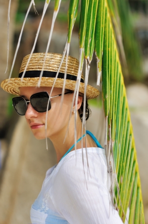 Woman in sunglasses near palm tree wearing hatの写真素材