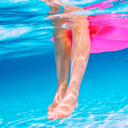 Woman relaxing on inflatable mattress at the beach, view from underwater
