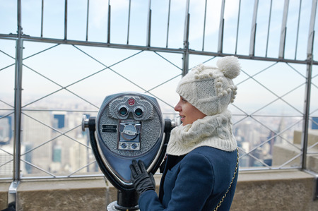 Woman in New York City with binoculars and Manhattan skyline at background
