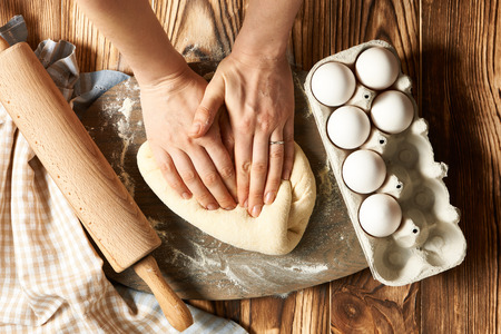 Female hands kneading dough on wooden table