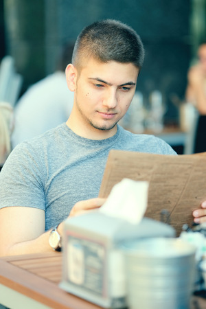 Young man in outdoor restaurant looking at the menuの写真素材