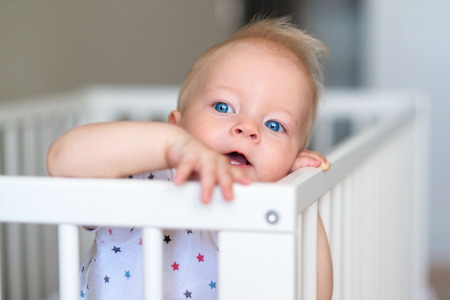 Baby boy with blue eyes standing in cribの写真素材
