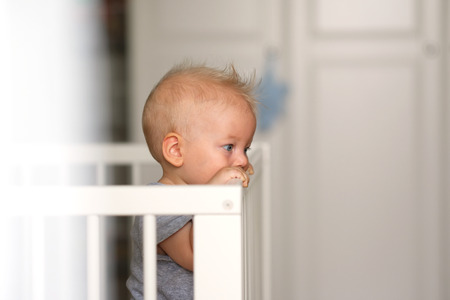 Baby boy with blue eyes standing in cribの写真素材