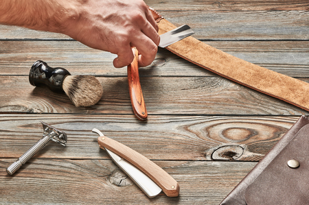 Man stropping straight razor with leather tool against old wooden backgroundの写真素材