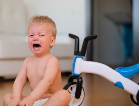 Baby boy crying sitting on floor. Bicycle in backgroundの写真素材