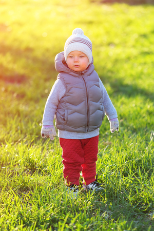 Portrait of toddler child in warm vest jacket outdoors. One year old baby boy wearing vest jacket at park meadow during sunset.の写真素材