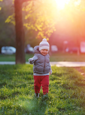 Portrait of toddler child in warm vest jacket outdoors. One year old baby boy wearing vest jacket at park meadow during sunset.の写真素材