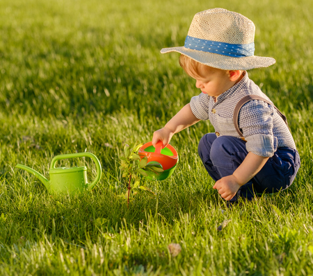 Portrait of toddler child outdoors. Rural scene with one year old baby boy wearing straw hat using watering canの写真素材